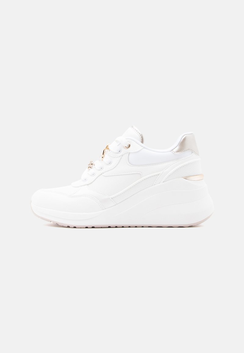 Chaussure de sport blanche avec une tige en cuir lisse et textile, une semelle compensée surélevée, et des accents métalliques au niveau du talon et des lacets.