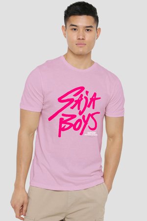 Young man wearing a light pink T-shirt with bold hot pink text "Saija Boys" and small "K-Pop Demon Hunters" logo, beige pants, neutral background.