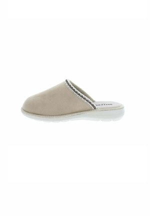 Zapatilla de estar por casa beige, cerrada por delante, con ribete decorativo y una suela blanca gruesa, mostrada de perfil sobre un fondo blanco.