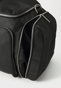 Zaino nero realizzato in tessuto liscio con doppie cerniere argento, dotato di due tasche esterne e di un corpo imbottito per garantire struttura.