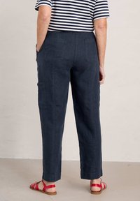 Navy linen blend pants with a straight cut, two side pockets, and two back pockets. Worn with red strappy sandals on a neutral floor.