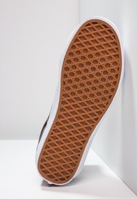 Semelle de chaussure de sport en caoutchouc avec un motif texturé en nid d'abeilles. Flancs blancs, dessous en caoutchouc marron, montrant adhérence et durabilité.