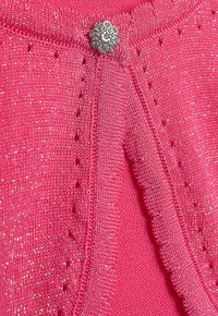 Rosa gestrickte Strickjacke mit strukturiertem Finish, dekorativem silbernem Knopf und gewellten Kanten. Funkelnde Fäden, die eingewoben sind.