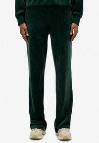 Donkergroene velours broek met een zachte textuur, voorzien van een relaxte pasvorm en subtiele geborduurde logodetails op de taille.