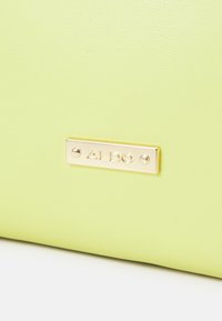Borsa sintetica verde lime con texture liscia; presenta una targhetta dorata con la scritta "ALDO". Design semplice senza ulteriori decorazioni.