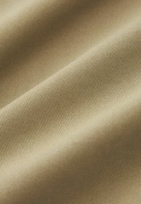 Beige tyg med en jämn, något strukturerad yta, som har fina diagonala ribbor och en subtil lyster. Mjuk fall ökar mångsidigheten.