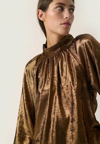 Blusa metallica marrone con colletto alto, dettagli arricciati al collo e maniche lunghe. Tessuto liscio e lucido con un motivo sottile.