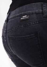 Jeans de denim gris oscuro con una vista en primer plano del bolsillo trasero y la etiqueta. La tela presenta una textura suave con sutiles detalles de costura.