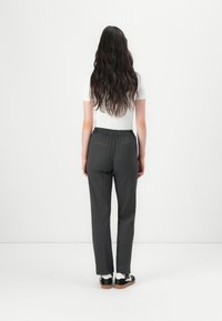 Pantalons gris ajustés avec une ceinture élastique, deux poches arrière et une coupe slim, associés à un haut blanc et des baskets noires.