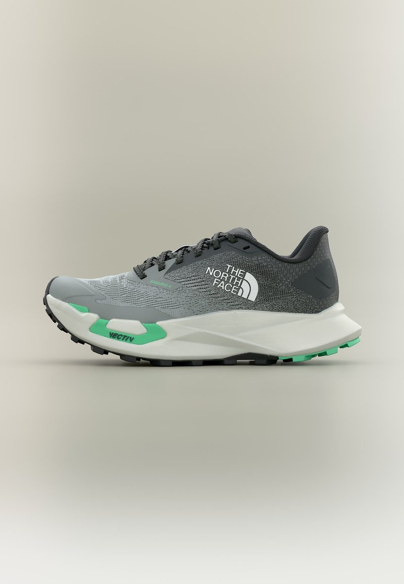 Γκρι και μαύρο παπούτσι για τρέξιμο σε μονοπάτια με λευκή σόλα, πράσινες λεπτομέρειες, το λογότυπο "The North Face" και μαύρα κορδόνια, σε πλάγια όψη.