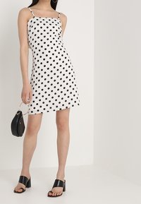 Robe à pois avec une silhouette ajustée, bretelles fines et un ourlet arrivant au genou, dans un schéma de couleurs noir et blanc.