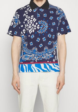 Short-sleeve polo shirt in dark blue featuring floral and animal prints. Accented with a black collar and a striped hem in light blue and white.