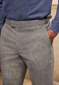 Pantaloni grigi a motivo con una texture liscia, frontale piatto e tasche laterali, abbinati a un maglione blu scuro in una vestibilità casual.