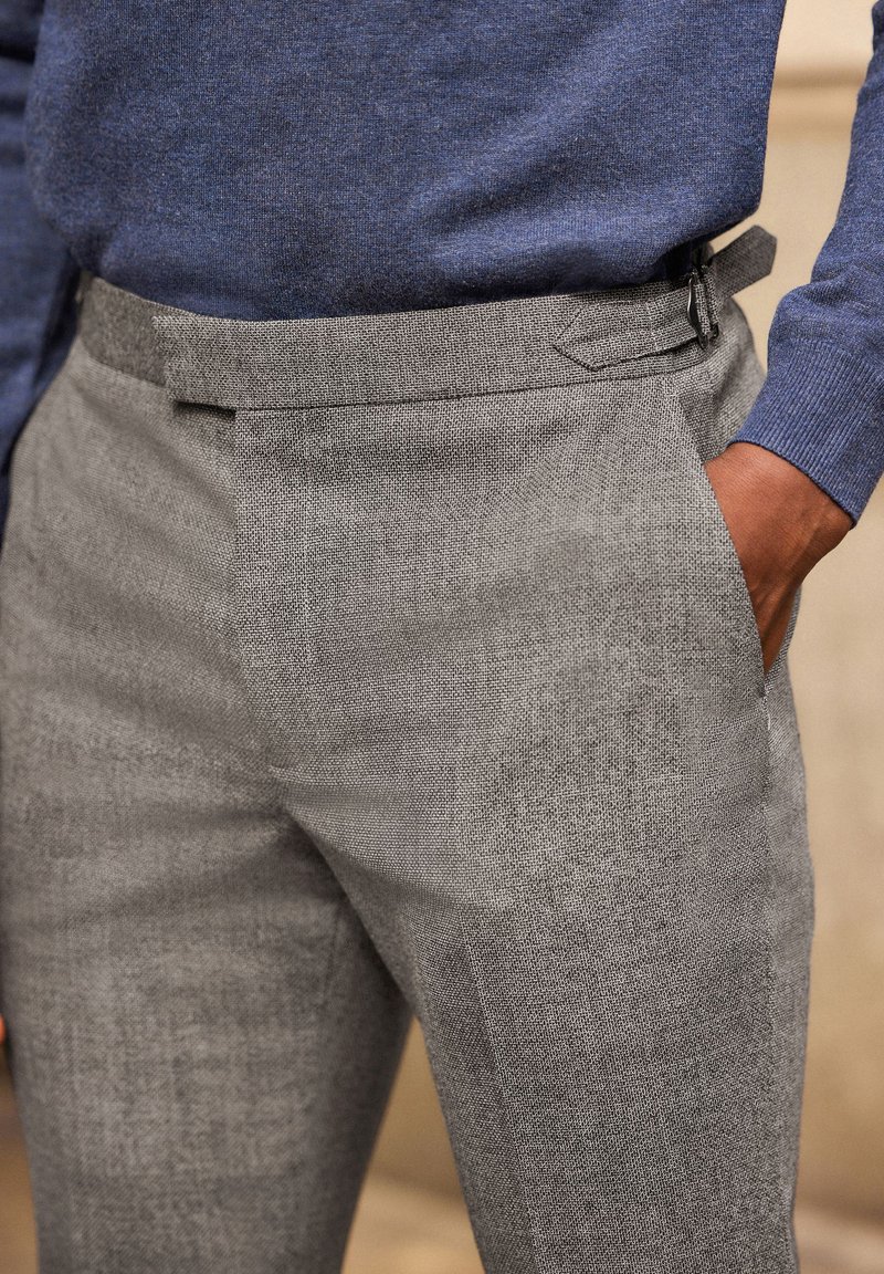 Pantaloni grigi a motivo con una texture liscia, frontale piatto e tasche laterali, abbinati a un maglione blu scuro in una vestibilità casual.