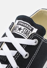 Schwarze Leinenschuhe mit weißer Gummisohle, weißen Schnürsenkeln und einem "Converse All Star" Logo auf der Zunge. Verzierende Nähte.