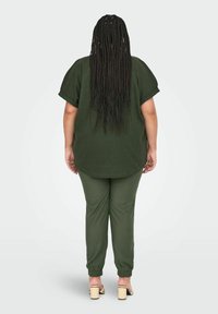 Grøn strikbluse med korte ærmer og afslappet pasform, parret med matchende tapered bukser. Materialet er blødt, med elastiske manchetter og slip-on hæle.