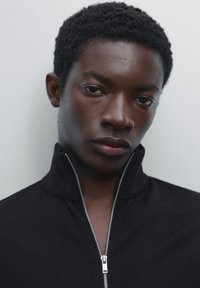 Black zip-up sweatshirt with a high collar, featuring a metal zipper and ribbed texture. The fabric appears smooth and fitted.