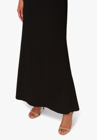 Schwarzes Maxikleid mit glatter Textur und ausgestelltem Saum, kombiniert mit hautfarbenen Rutschen mit minimalistischem Design und niedrigem Absatz.