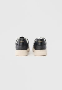 Μαύρα δερμάτινα sneakers με υφή, εκρού λεπτομέρειες και χρυσό λογότυπο στη φτέρνα. Σχεδιασμός με χαμηλό προφίλ και λαστιχένια σόλα.