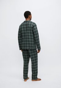 Pigiama a quadri verdi con maniche lunghe e pantaloni, caratterizzato da una vestibilità morbida e una texture soffice, visto da dietro.