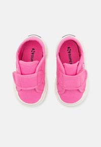 Světlé růžové dětské boty s texturovaným textilním svrškem a bílou gumovou podrážkou. Mají široký suchý zip pro snadné zapínání.