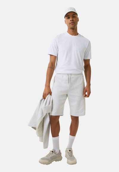 Lichtgrijze shorts en een wit T-shirt met subtiele branding, gecombineerd met een bijpassende grijze sweatshirt en beige sneakers.