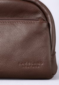 Brown leather toiletry bag with a textured finish, featuring a top zipper and embossed "Lakeland Leather" logo on the front.