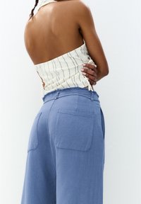 Jasny, prążkowany top na halter z odkrytymi plecami; luźne niebieskie spodnie z dwoma tylnymi kieszeniami i postrzępionym dołem.