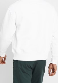 Weißes Sweatshirt mit rundem Ausschnitt und gerippten Bündchen, in lässigem Schnitt. Kombiniert mit dunkelgrünen Hosen, die ein einfaches Design zeigen.