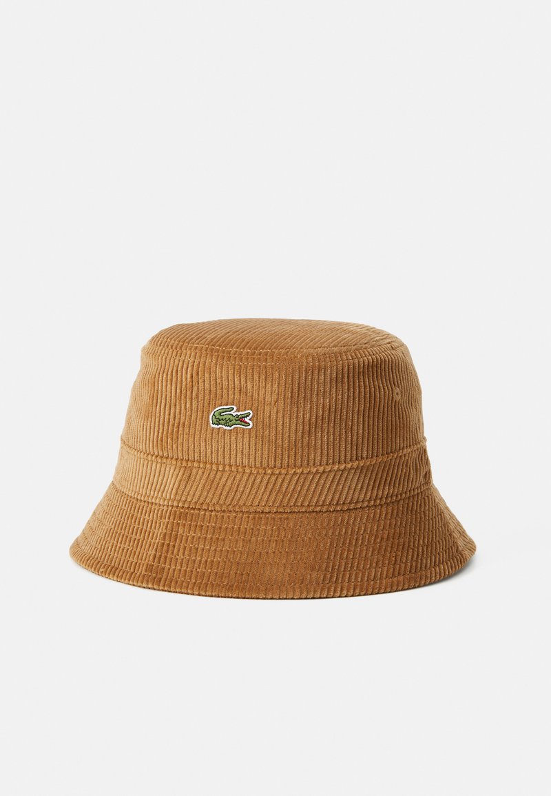 Cappello a secchiello in corduroy marrone con una texture a coste e un bordo leggermente largo. Presenta un piccolo logo di coccodrillo verde sul fronte.
