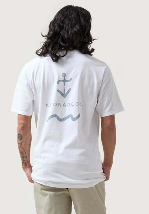 Camiseta de algodón blanca con un diseño gráfico en la parte posterior que presenta un símbolo de ancla y una línea ondulada en azul claro. Mangas cortas y un ajuste relajado.