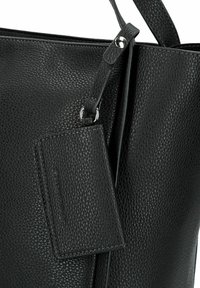 Sac fourre-tout en cuir noir avec une texture grainée, doté d'une étiquette détachable et d'une seule bandoulière. Comprend des accents en métal argenté.