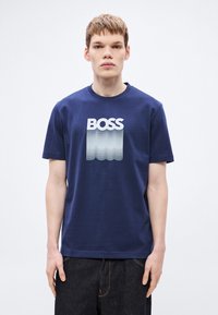 Temno modra bombažna majica z velikim belim napisom "BOSS" z valovitim gradientnim učinkom. Krožni izrez, kratki rokavi, standarden kroj.
