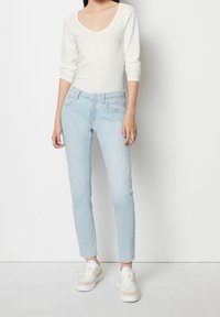 Svetle modré slim-fit džíny s pěti kapsami, zapínáním na knoflík a měkkou denimovou texturou, kombinované s bílým topem s dlouhým rukávem a teniskami.