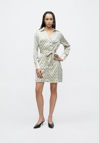 Ilgas rankovėmis šviesios spalvos šilkinė suknelė su geometriniu raštu, su diržu ties juosmeniu ir kontrastinėmis atlasinėmis rankogaliais. Dėvima su juodais smailiais kulniukais.