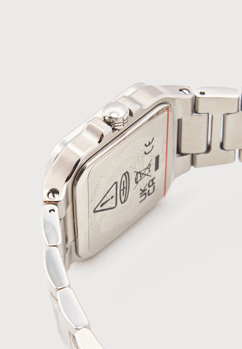 Stainless steel wristwatch with metal link band, showing the back case with warning symbols and a side crown on a white background.