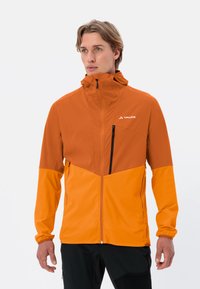 Veste orange avec une partie inférieure orange plus clair, fermeture éclair à l'avant, col haut et poche poitrine zippée. Présente des poignets élastiques.