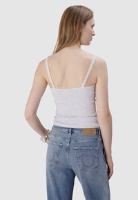 Szary top na ramiączkach z cienkimi paskami, koronkowym wykończeniem, połączony z jasnoniebieskimi dżinsami z haftowanymi tylnymi kieszeniami i brązową skórzaną naszywką.