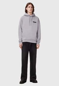 Grijze katoenen hoodie met een voorste kangoeroezak, een capuchon met trekkoord en een klein zwart logo op de borst, gecombineerd met zwarte wijde jeans.