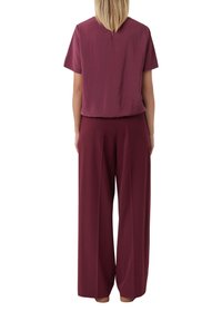 Top borgogna con maniche corte e una vestibilità ampia, abbinato a pantaloni larghi in coordinato dello stesso colore. Tessuto morbido e dalla texture uniforme.