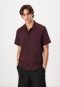 Korte mouwen, bordeauxrood shirt met een gestructureerd patroon, knoopsluiting en kraag. De stof lijkt lichtgewicht en soepel te zijn.