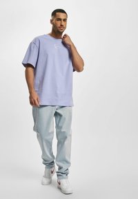 Lavendel kortærmet skjorte med rund hals, parret med lyseblå jeans og hvide sneakers med røde accenter. Enkel design, afslappet pasform.