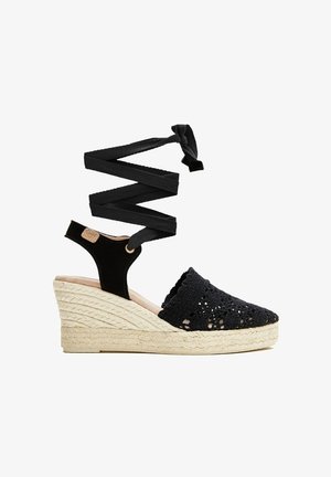 Alpargata negra tejida con cuña, puntera cerrada, cintas para atar en el tobillo y plataforma con tacón de yute trenzado.