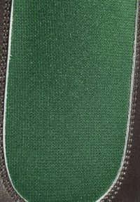 Zapato negro con una sección de tela texturizada de color verde oscuro. Los bordes están cosidos cuidadosamente con un hilo blanco en contraste.