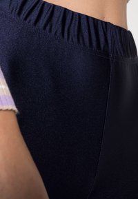 Tmavě modré legíny s vysokým pasem a hladkým, lesklým povrchem. Elastický pas, shromážděný detail a viditelné ploché švy.