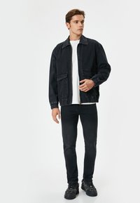 Chaqueta de denim oscuro con cierre de cremallera en la parte delantera, dos bolsillos en el pecho, puños elásticos y un corte relajado, combinada con unos jeans negros y zapatillas oscuras.