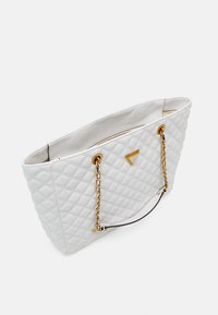 Quiltet hvid tote taske med kædehåndtag i guldtoner, en trekantet logoaccent og et rummeligt interiør med lynlås. Glat tekstur.