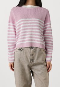 Pull en tricot rayé rose et blanc avec un col rond et un ourlet côtelé. Associé à un pantalon en denim de couleur claire.