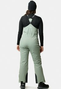 Gröna snöbyxor i overallstil med justerbara remmar, figurnära midja, stora fickor och förstärkta svarta detaljer vid anklarna.