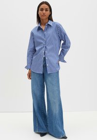 Blau-weiß gestreiftes Hemd mit Knöpfen und langen Ärmeln, kombiniert mit weiten, hellblauen Jeans und schwarzen High Heels. Glatte Stofftextur.